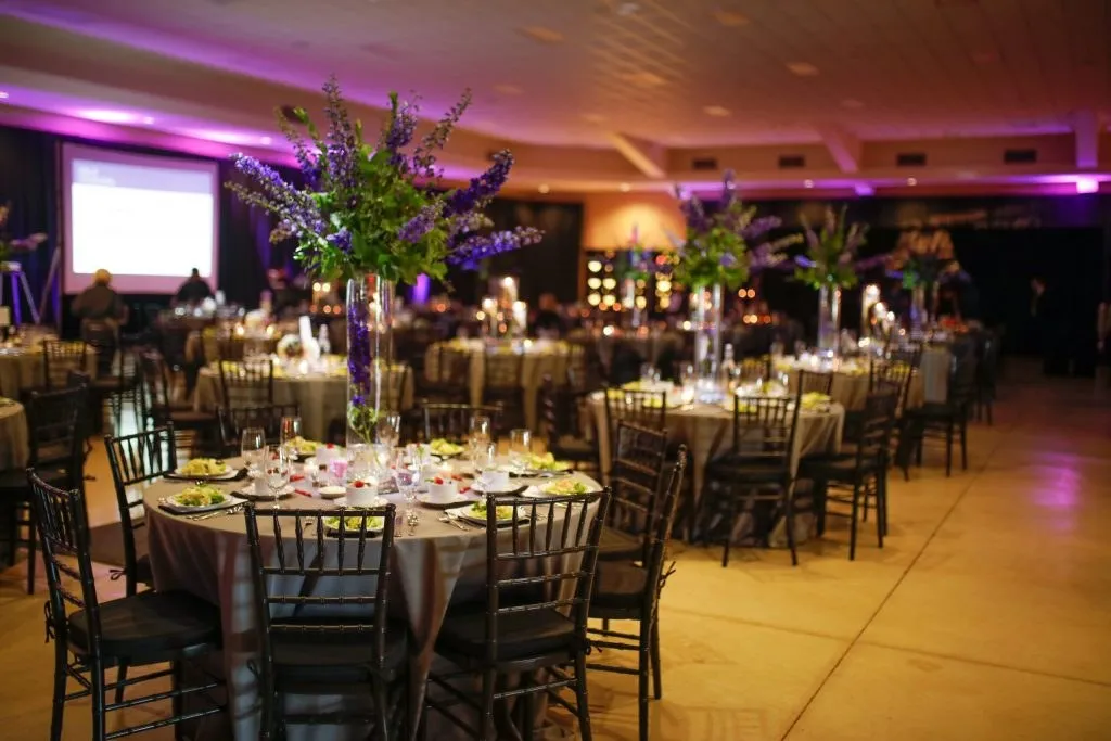 Banquet room set with round tables, centerpieces, uplighting and a projection screen