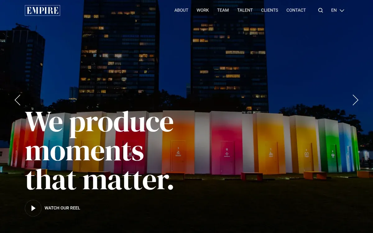 Empire Entertainment homepage hero with the Empire wordmark and the headline We produce moments that matter over a night photo of a row of brightly colored panels on a lawn below city towers, with a Watch our reel button