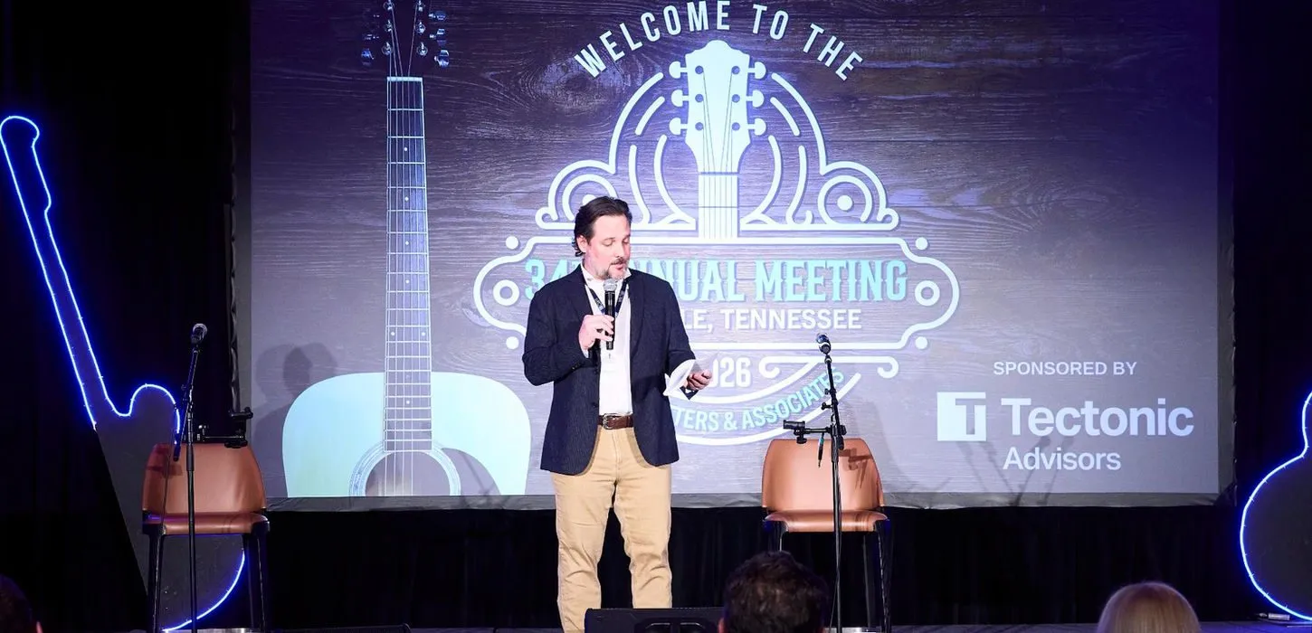 Speaker on a lit stage in front of a large welcome screen at a corporate event