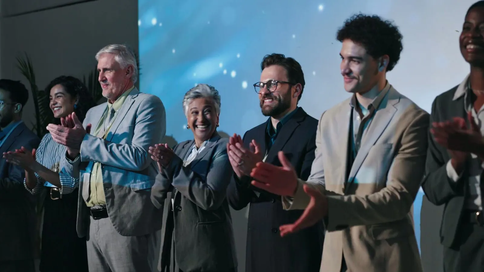 Attendees applauding in front of a lit stage backdrop at a corporate event