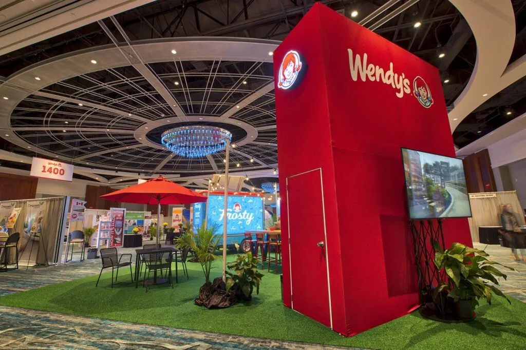 Branded exhibit booth with a tall feature structure and landscaped seating