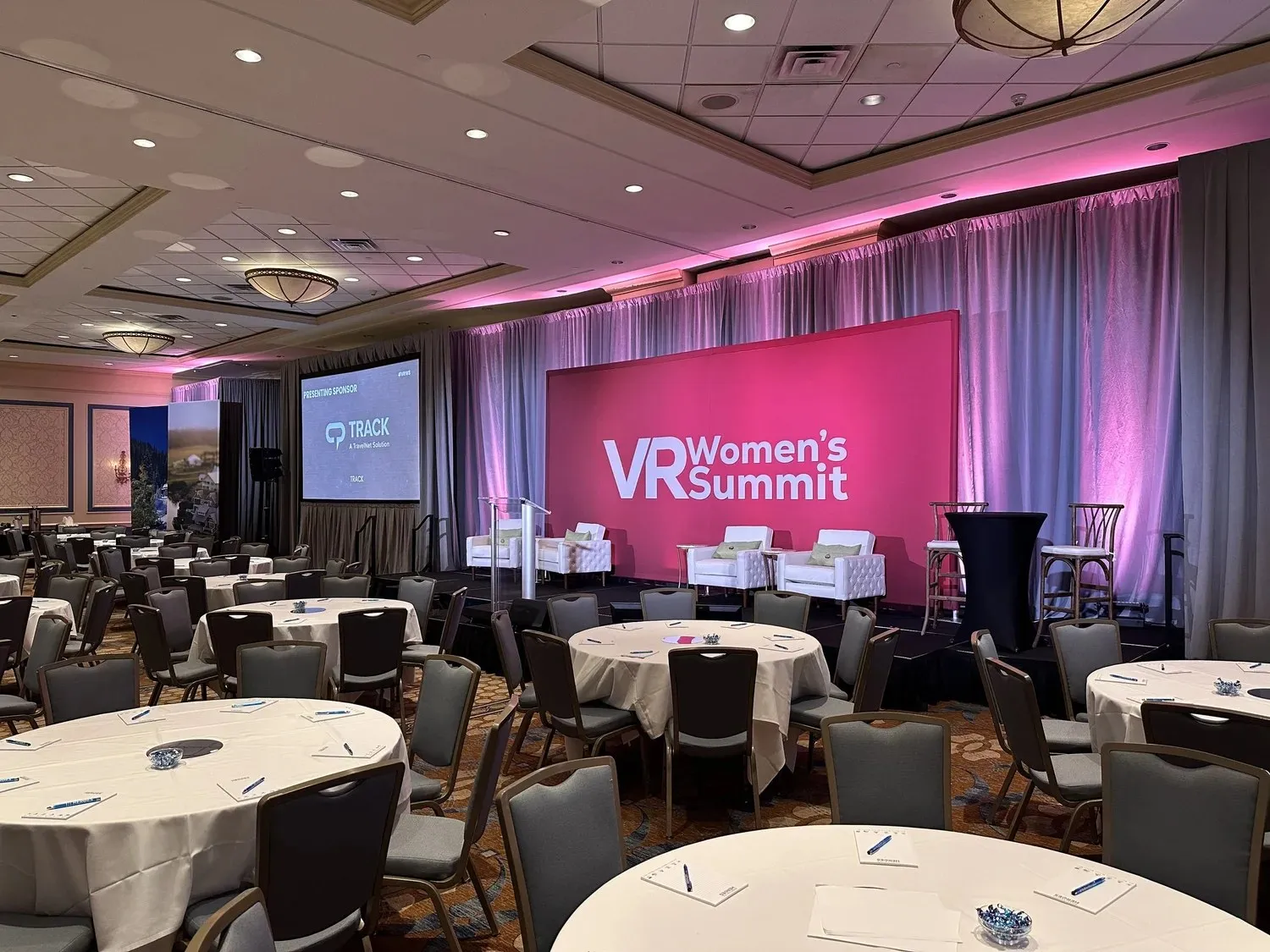 Summit stage with a pink-lit backdrop and side screens above round tables