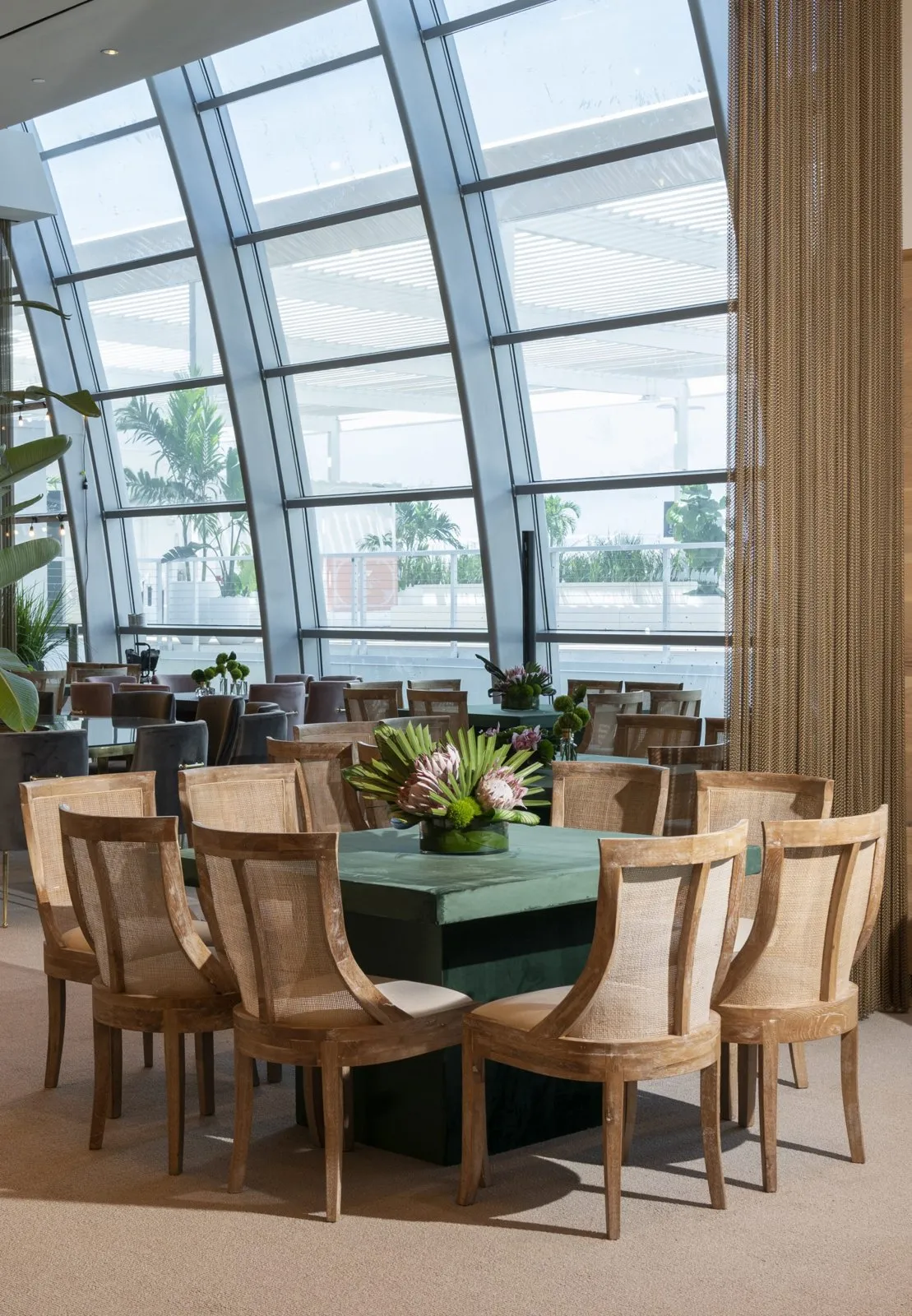 Dining table with a floral centerpiece beside floor-to-ceiling windows