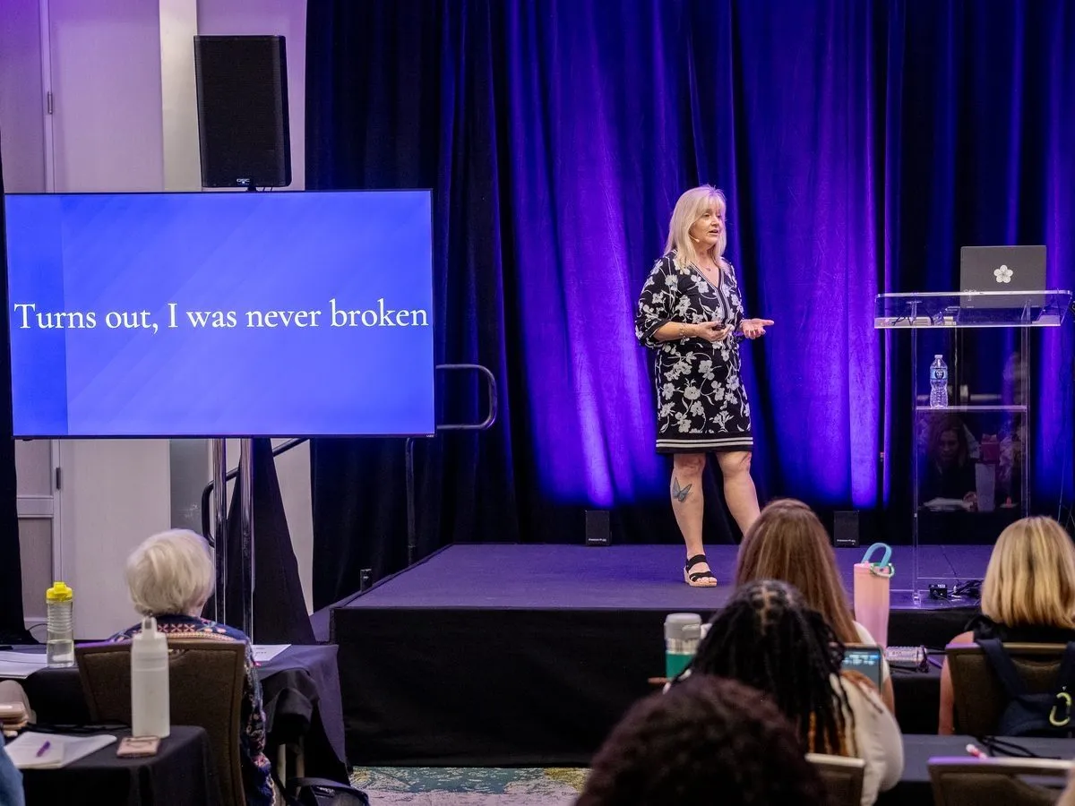 Keynote speaker on a stage with purple lighting and a presentation screen