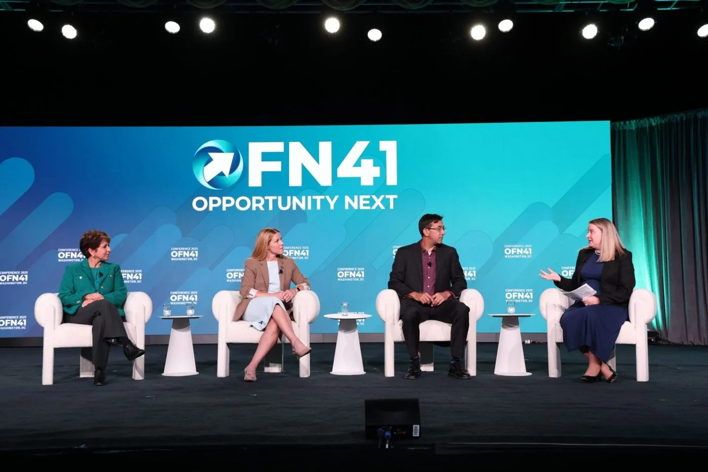 Four panelists seated on a conference stage in front of a large screen