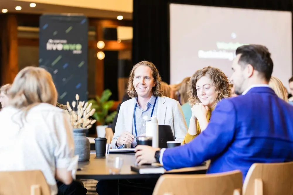 Attendees seated at a table with lanyards listening to a session