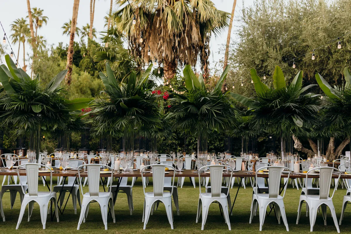 Long outdoor dinner tables among palms at a Palm Springs event