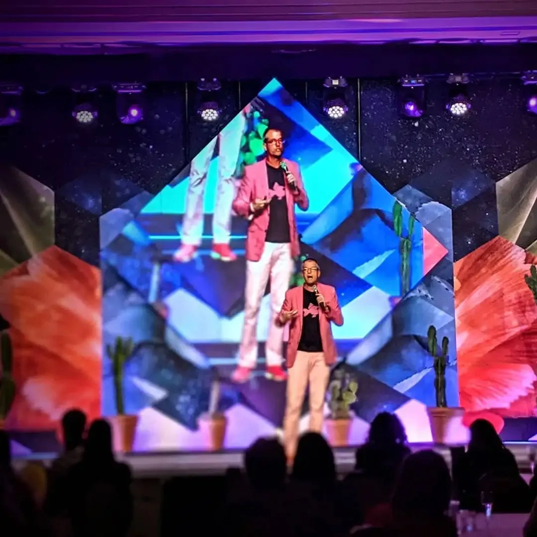 Two presenters on stage in front of an LED wall with live video, produced by Commotion Studios