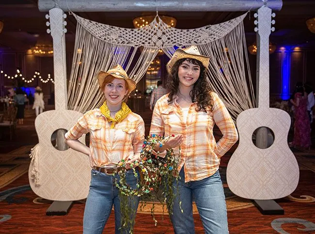 Two guests in western wear at a themed photo backdrop with guitar decor