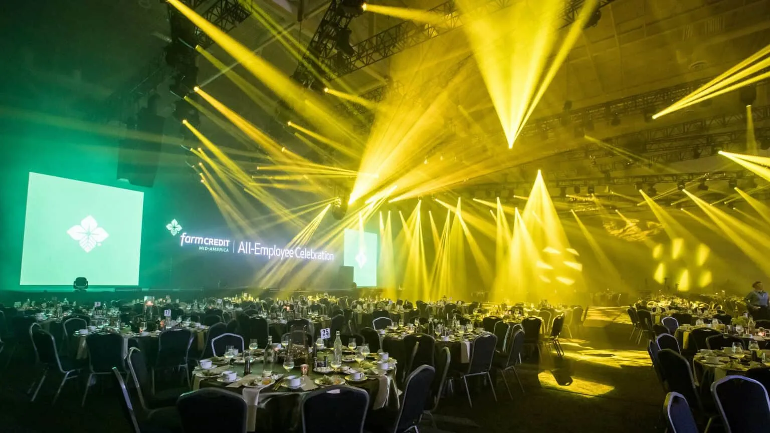 Round dinner tables in a ballroom with stage lighting beams overhead