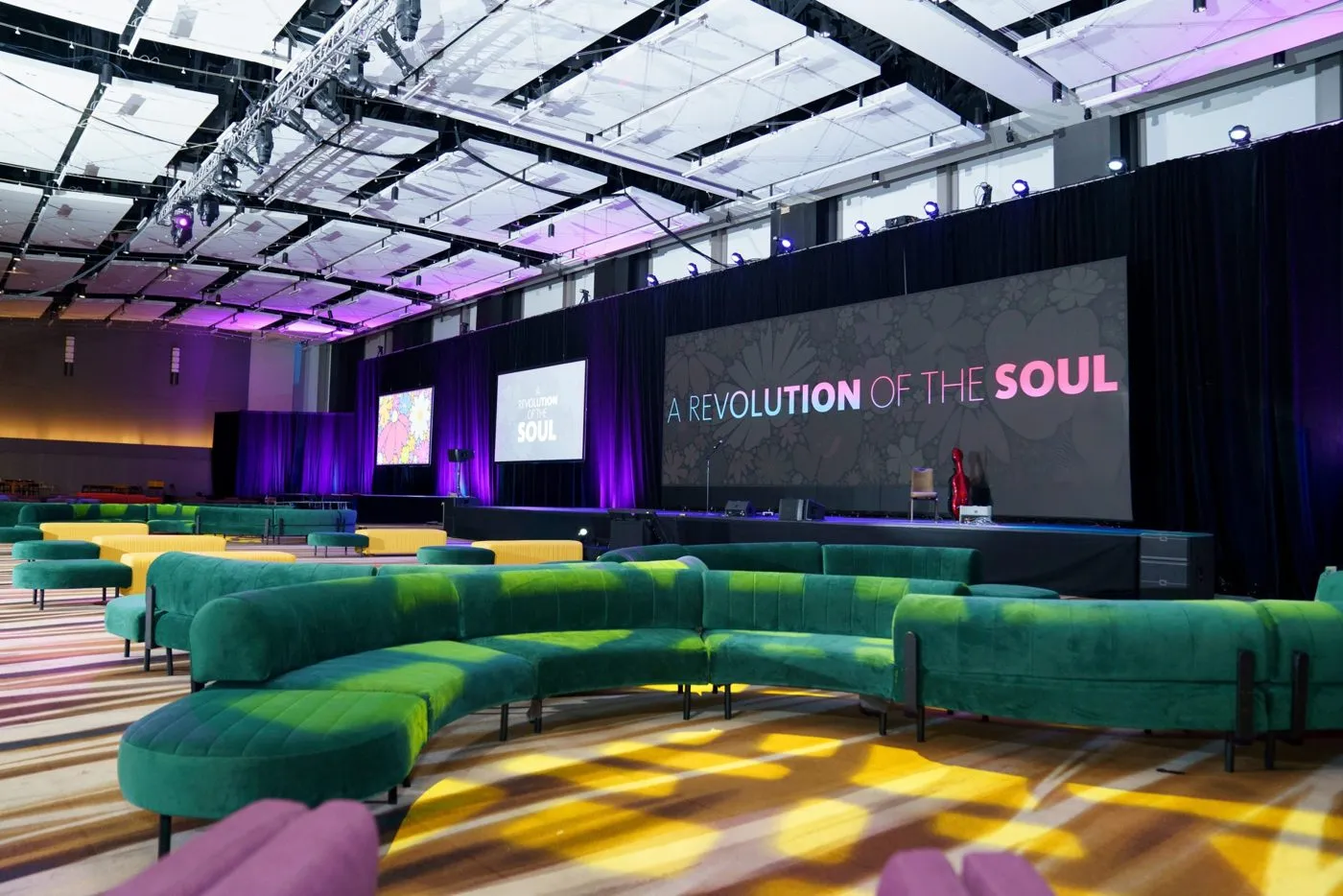 Ballroom set with green sofa lounge seating and a stage with screens