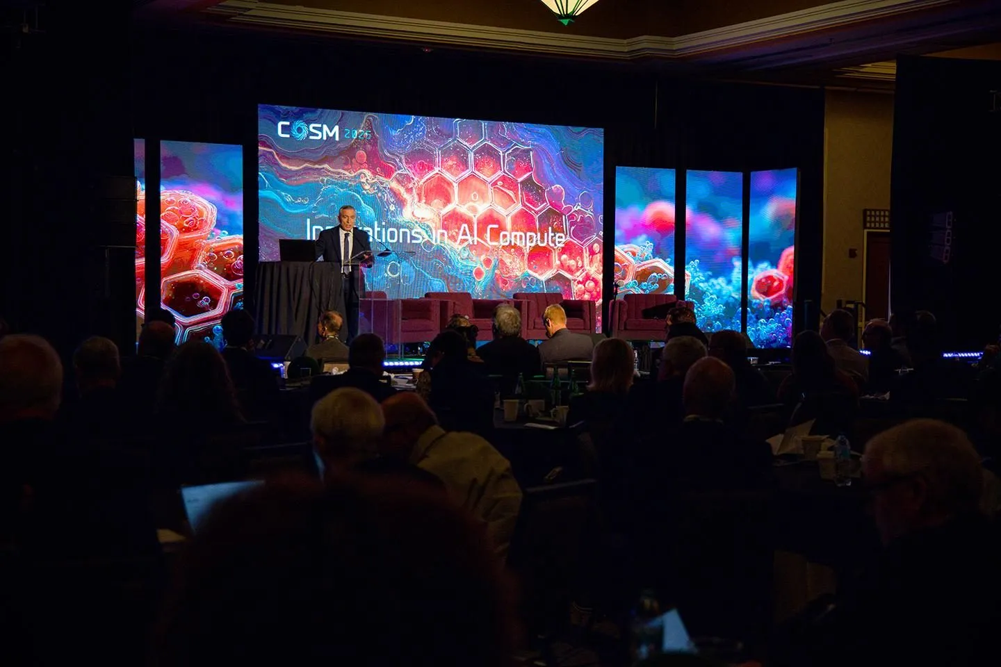Audience facing a lit conference stage with LED screens