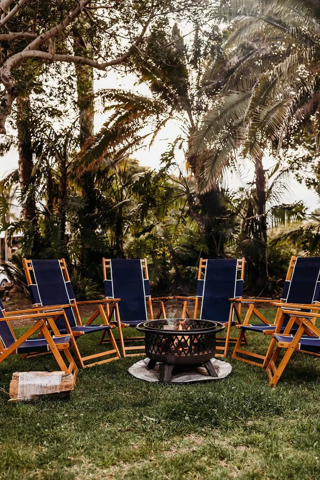 Navy Adirondack chairs around a fire pit on a palm-lined lawn at the San Diego retreat