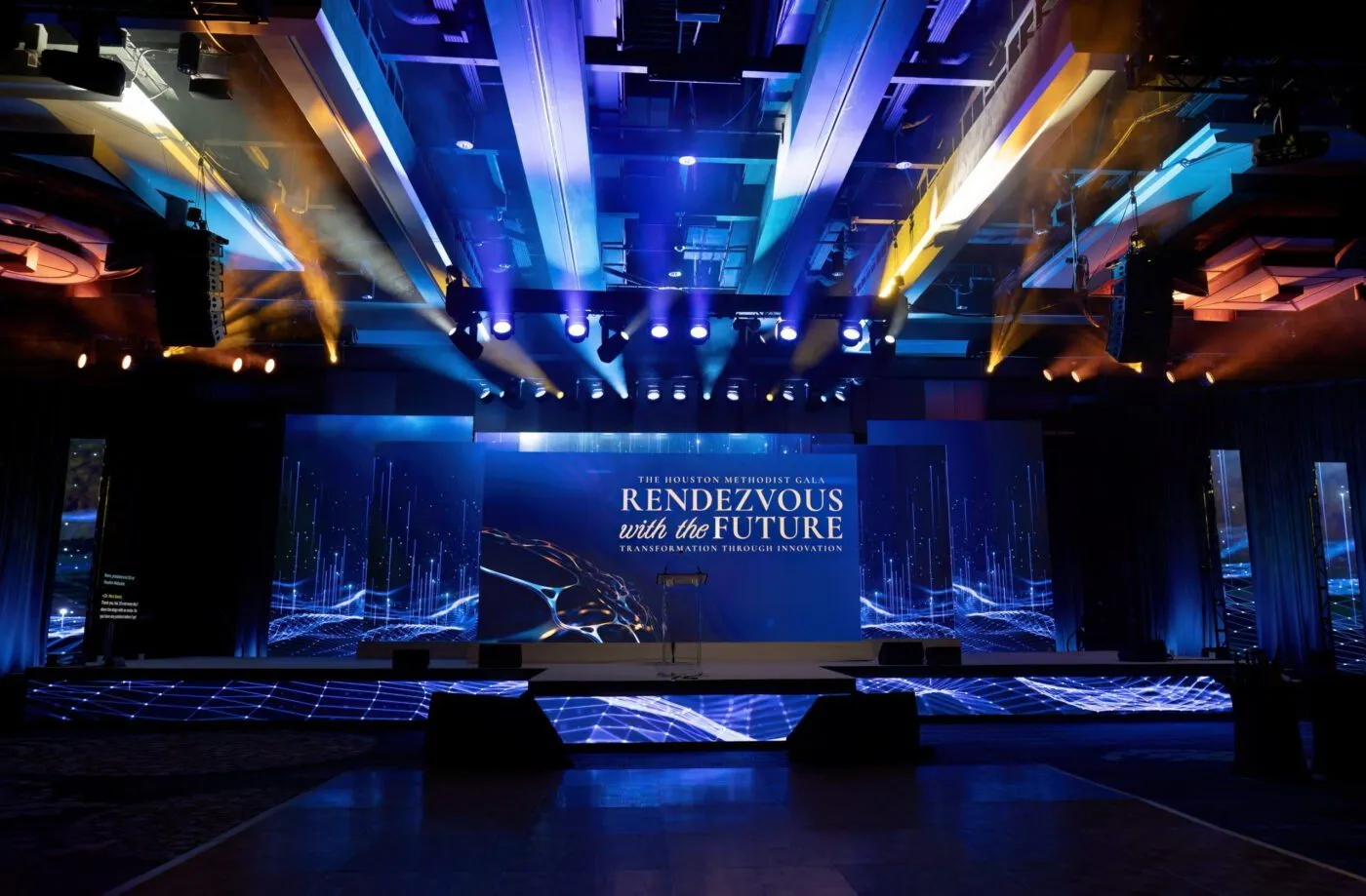 Blue lit stage set for a corporate event with a branded backdrop