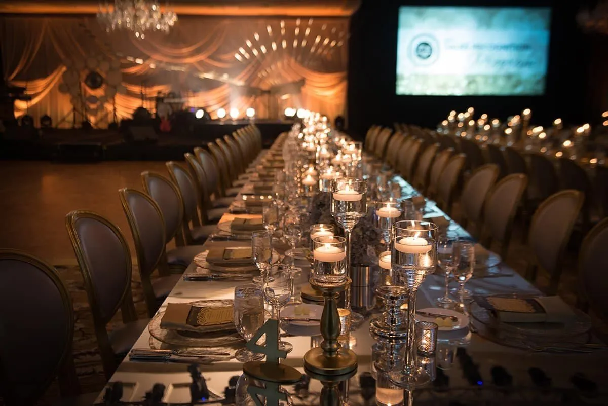 Long banquet table with candles in front of a presentation screen at a gala