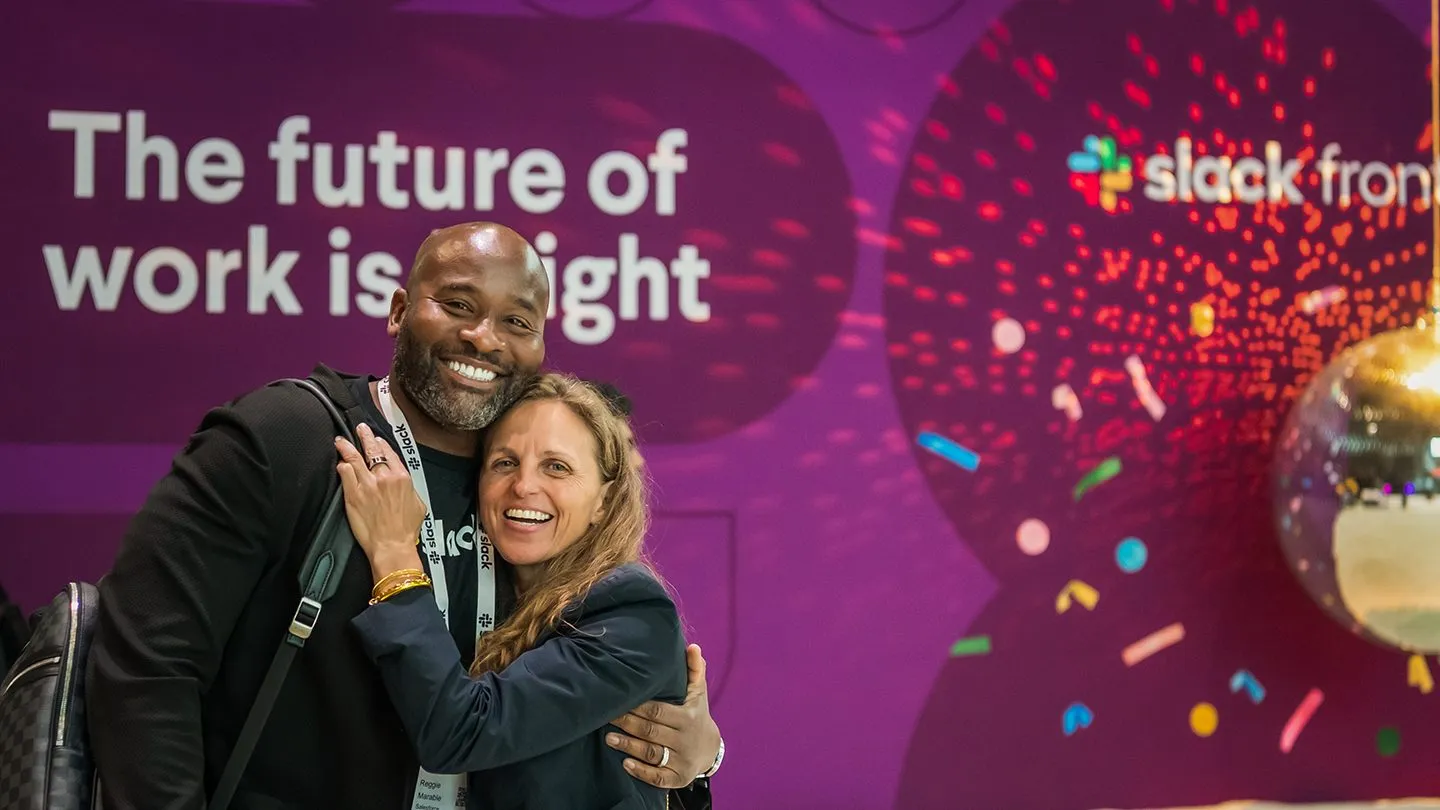 Two attendees posing in front of a stage backdrop at a customer conference