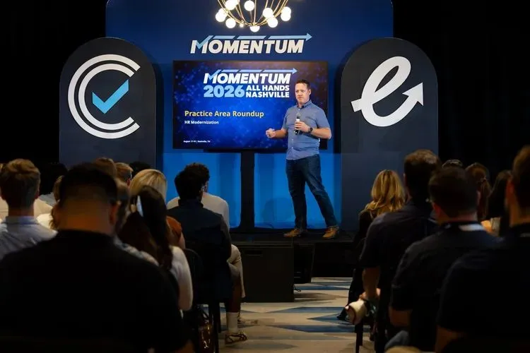 Speaker on stage at a branded all hands event with logo screens