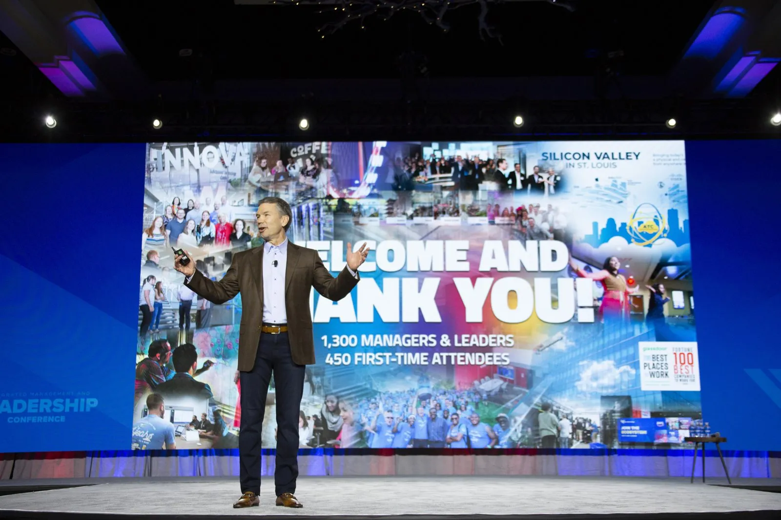 Presenter on stage in front of a large welcome and thank you screen