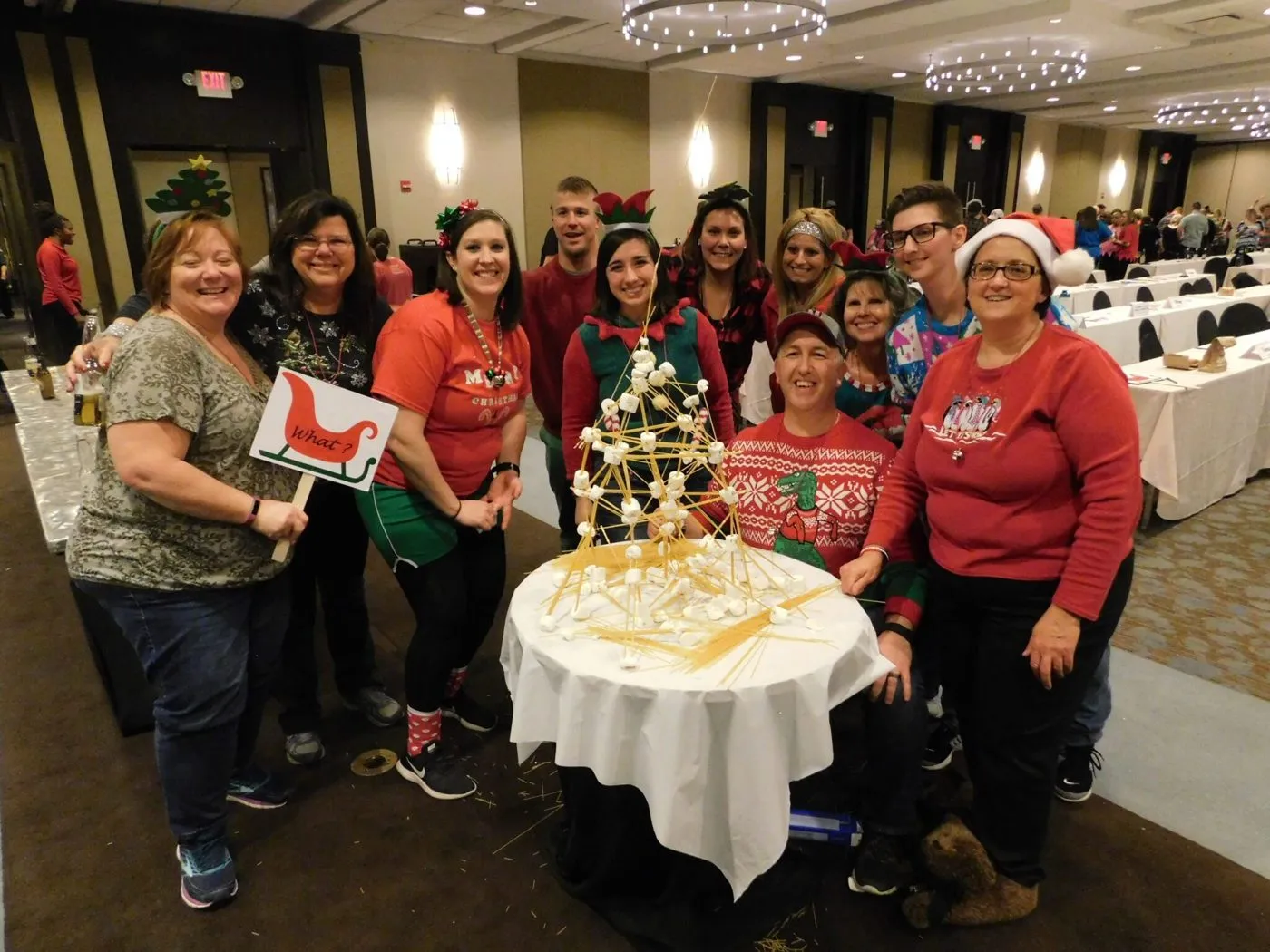Employees in holiday sweaters gathered around a decorated table at a team building event