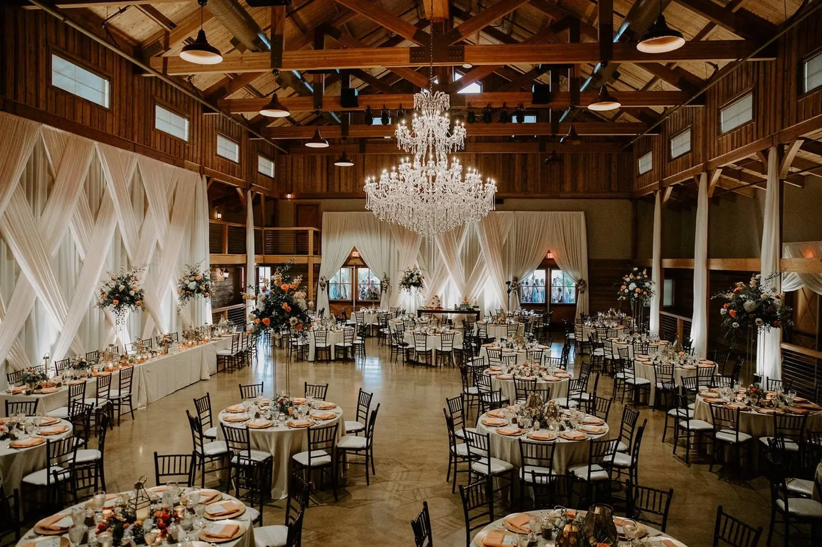 Timber-beamed event hall set for dinner with chandeliers and draped walls