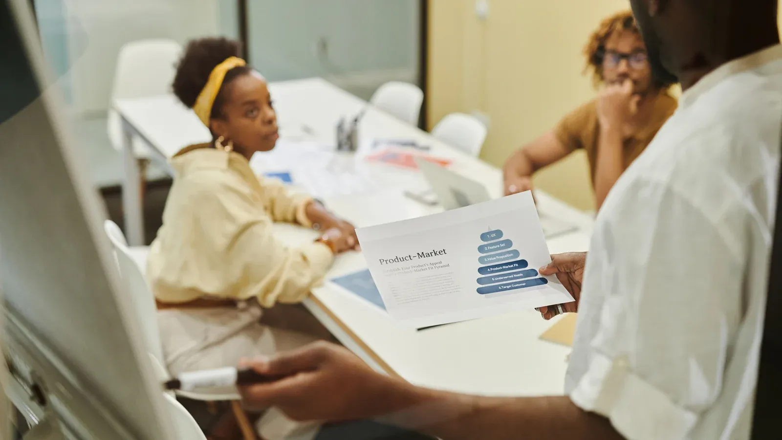 Colleagues review a printed chart together around a white meeting table. One woman listens as a teammate points to the figures.