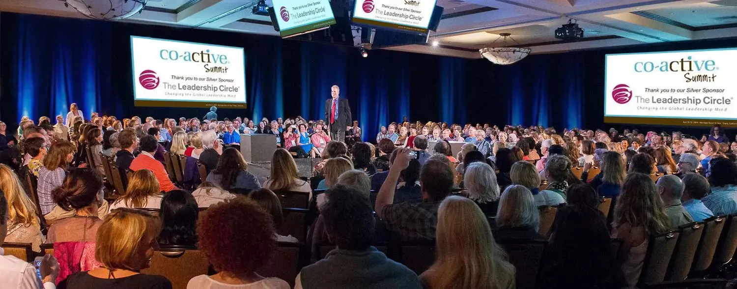 Large audience seated in a hotel ballroom for a corporate conference session