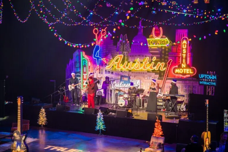 Band performing on a lit stage with a neon Austin sign at an event