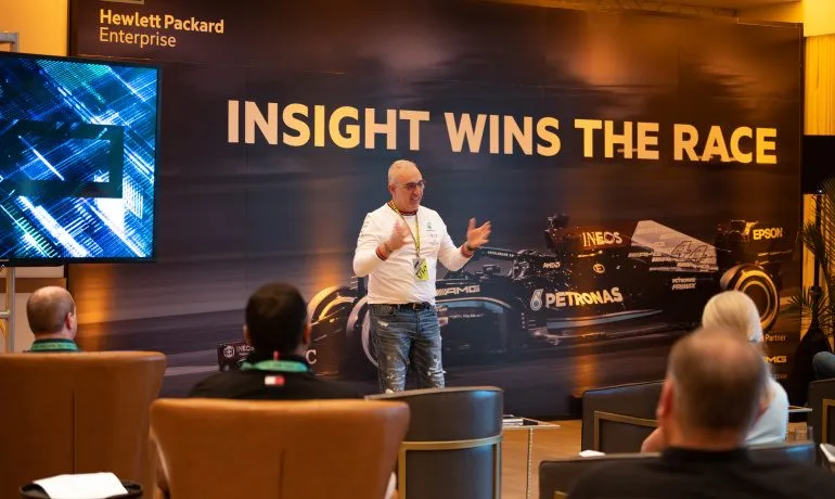 Presenter on stage in front of a lit screen at a motorsport themed customer event