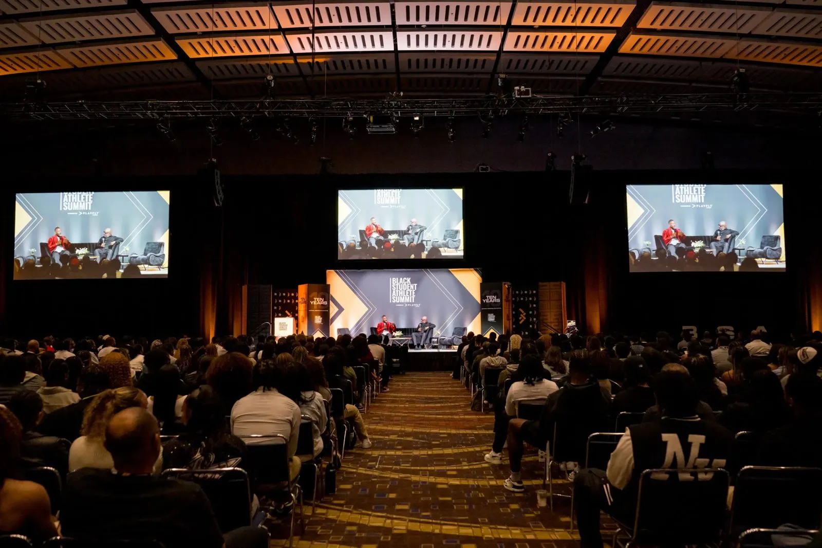 Conference audience seated in a hall with presentation screens