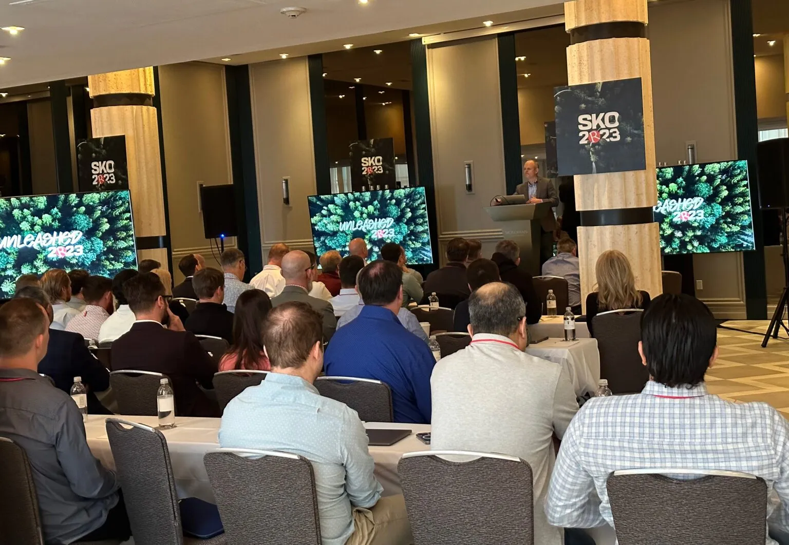 Attendees seated at tables in a ballroom with screens for a sales kickoff