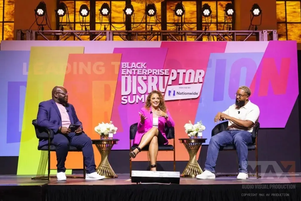 Three panelists seated on a branded summit stage with large video screens