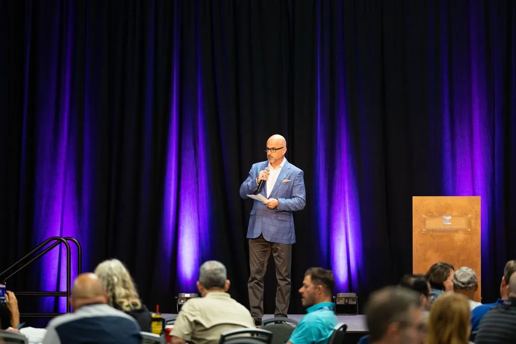 Speaker on stage in front of a purple curtain at an industry summit