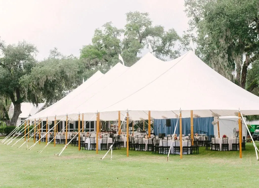 Sailcloth tent set for dinner on a lawn under live oaks