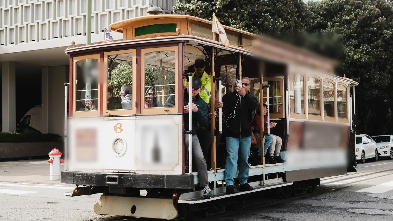 A group rides the running boards of a classic cable car along a sunny street during an incentive trip in San Francisco.