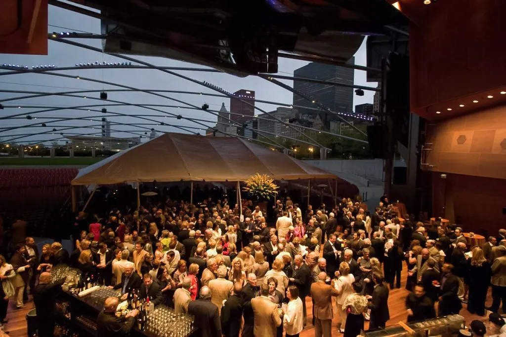Guests at tables under a tent beside a Chicago park pavilion