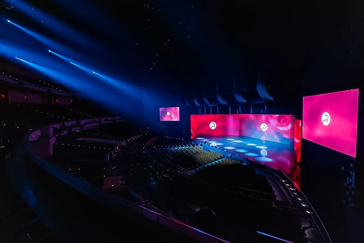 Large conference stage with lit screens seen from the upper seating
