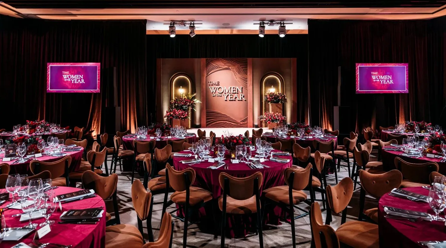 Dinner tables set under pink lighting in a dark venue