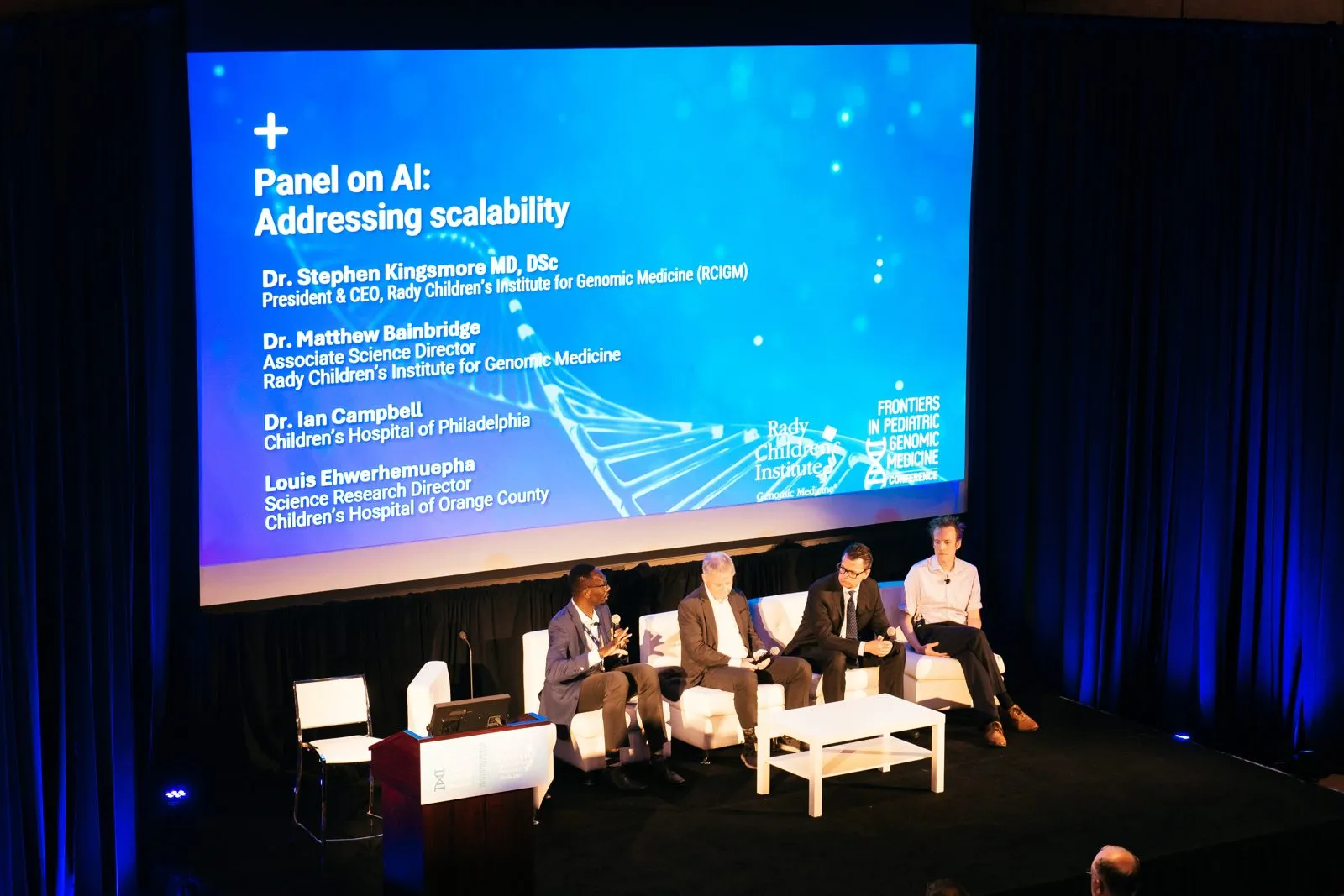 Panel discussion on stage in front of a presentation screen at a conference