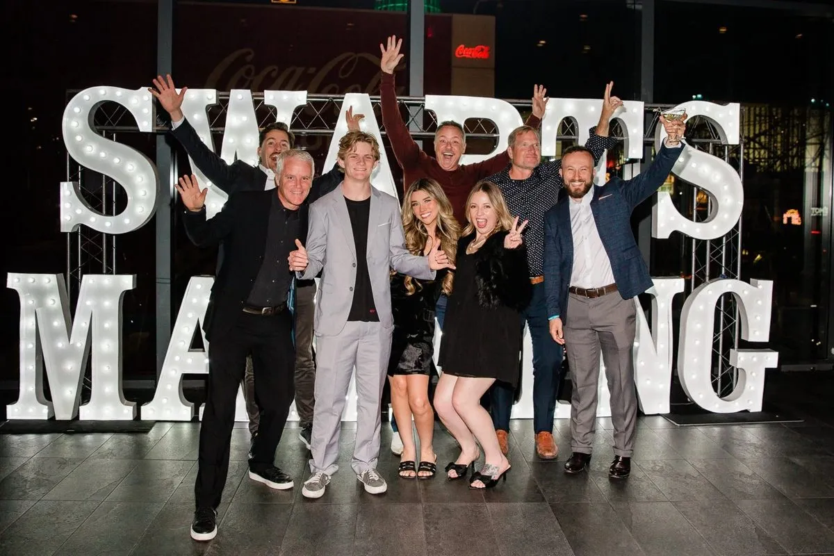 Group celebrating in front of illuminated Swarts Manning letters