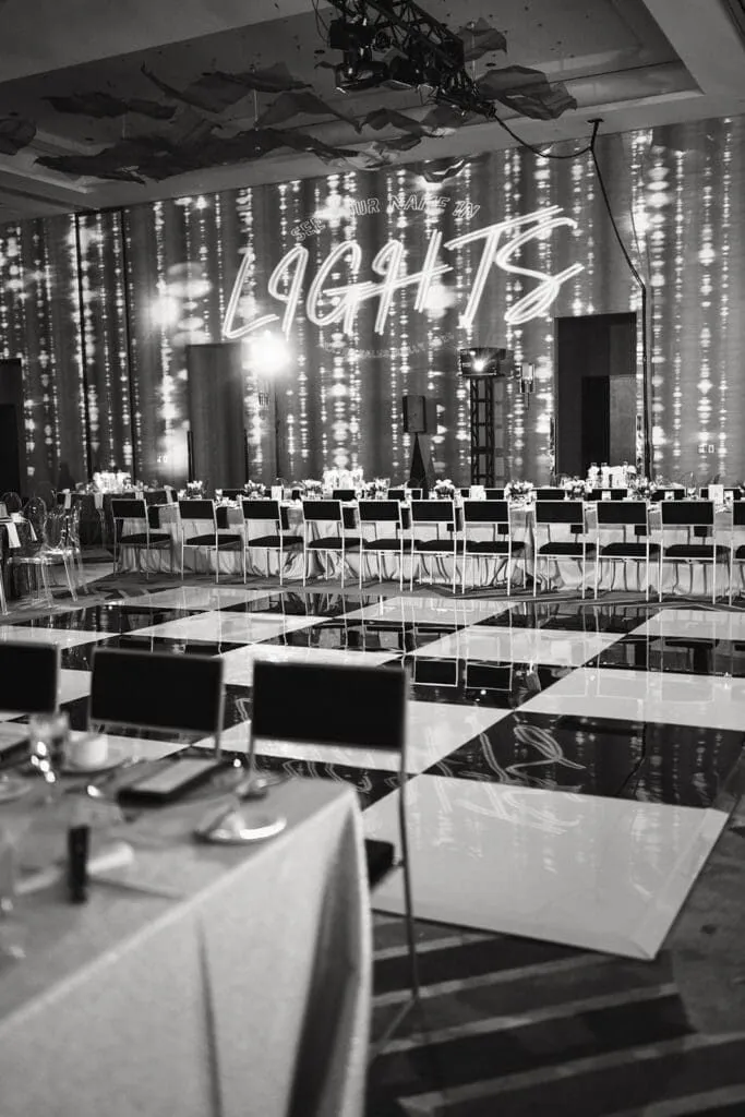 Black and white view of banquet tables with centerpieces and stage lighting