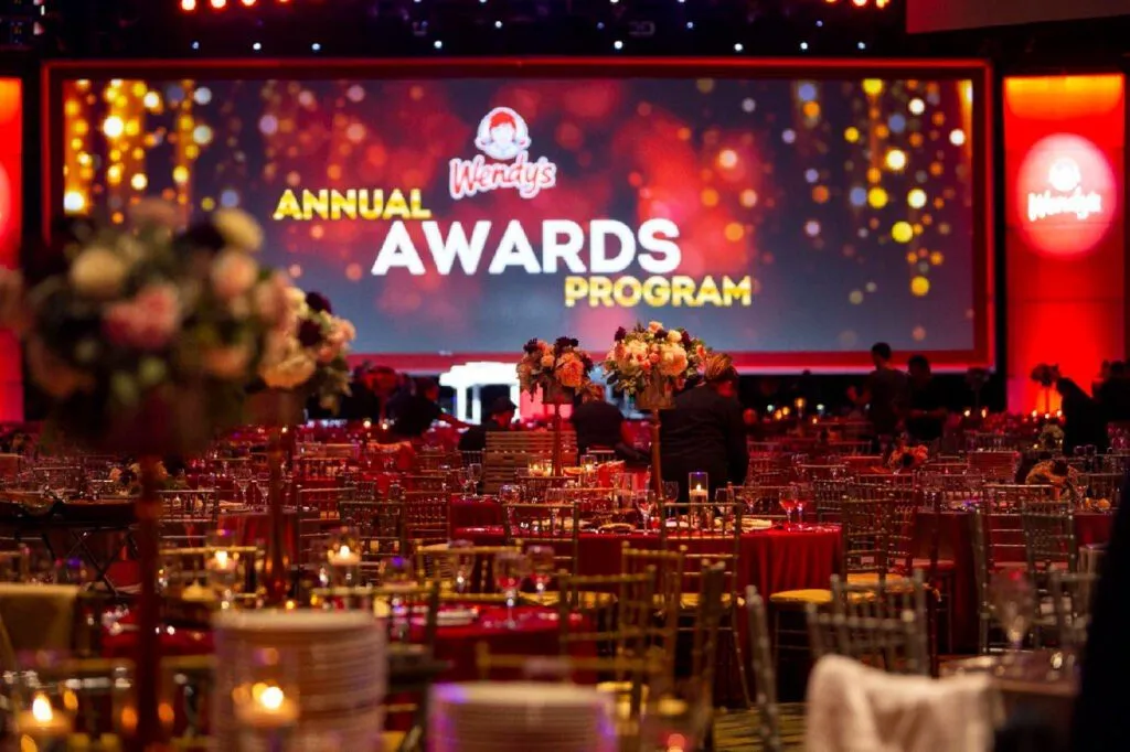 Awards program in a ballroom with decorated dinner tables and a large stage screen