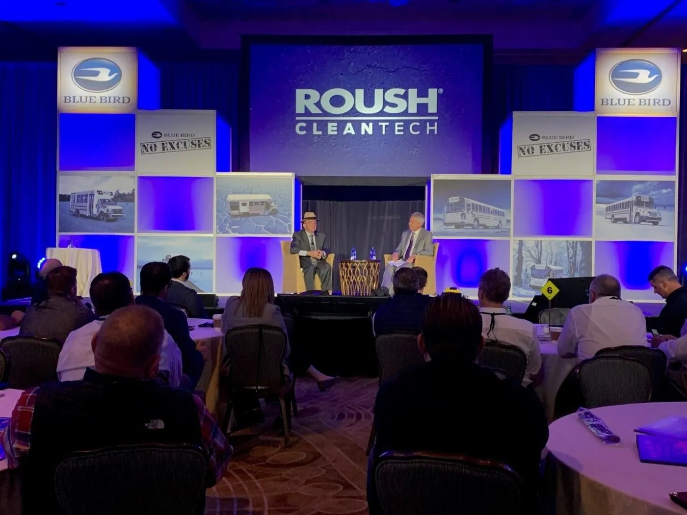 Attendees seated at a corporate meeting with branded screens on stage