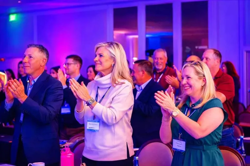 Conference attendees with name badges applauding in a lit event room
