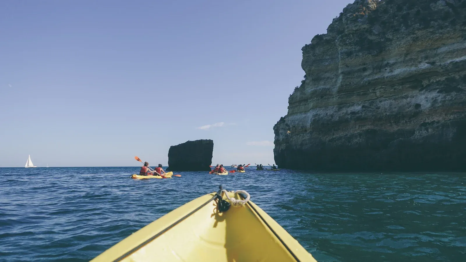 A group paddles bright sea kayaks past towering coastal cliffs on a sunny outing during an incentive trip.