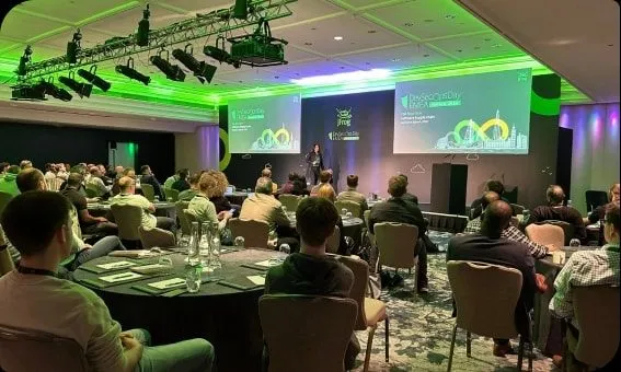 Attendees at round tables facing a green lit presentation screen