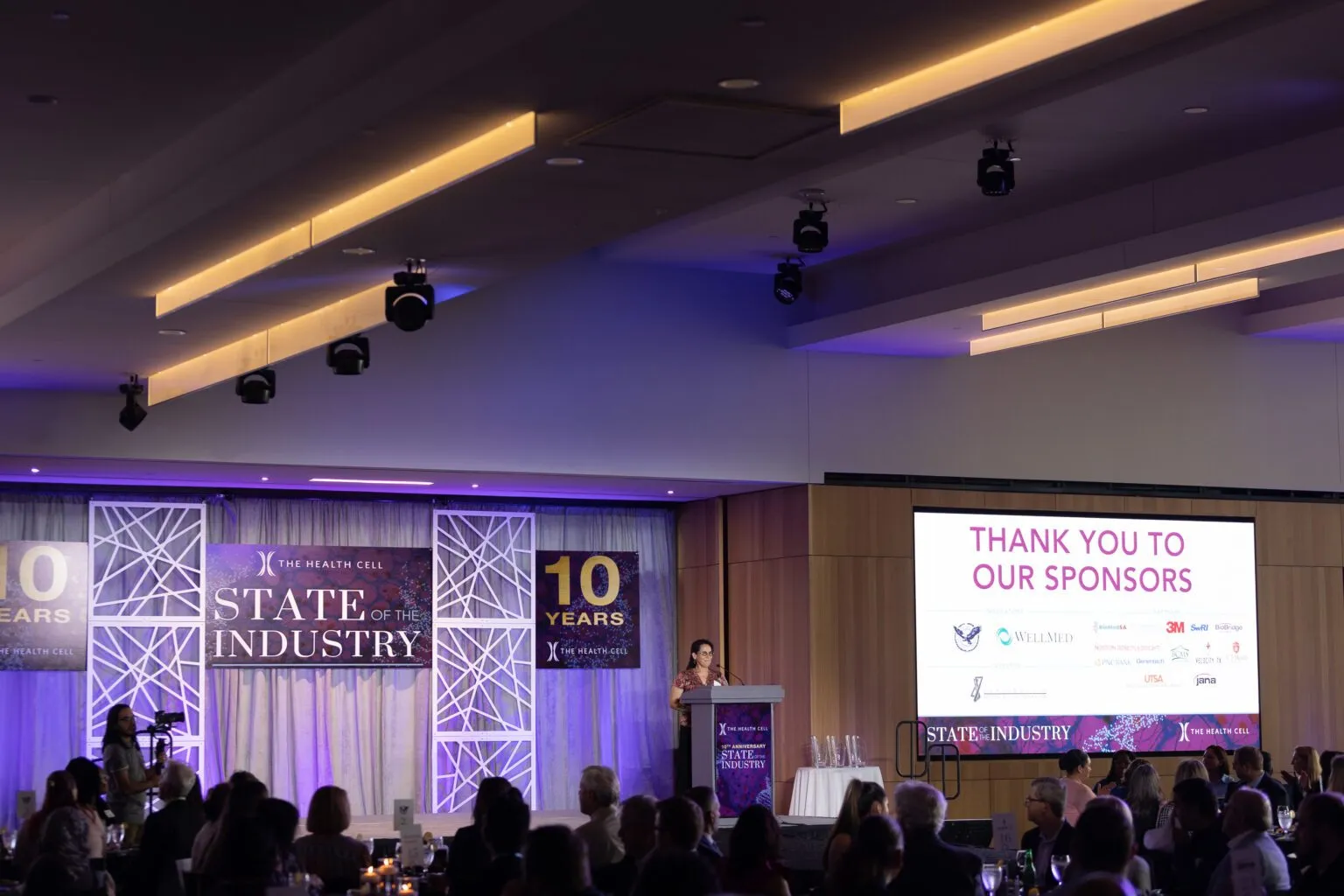 Ballroom filled with attendees facing screens and a branded stage