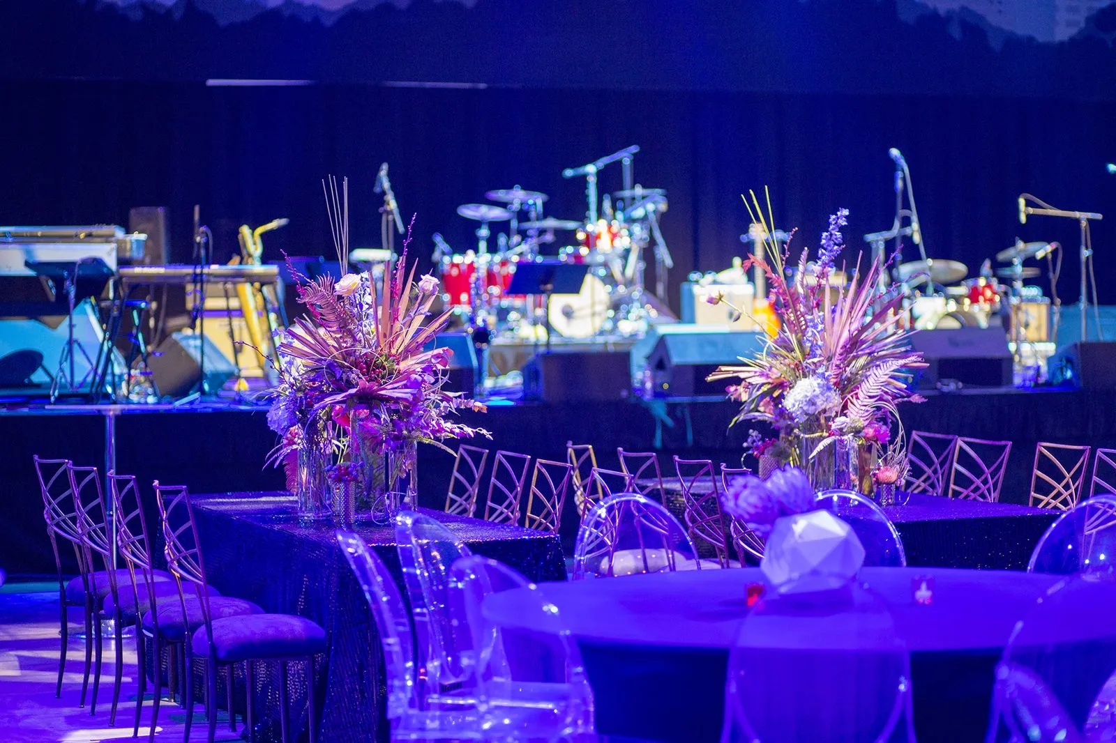 Round tables with floral centerpieces in front of a band stage at a company reception