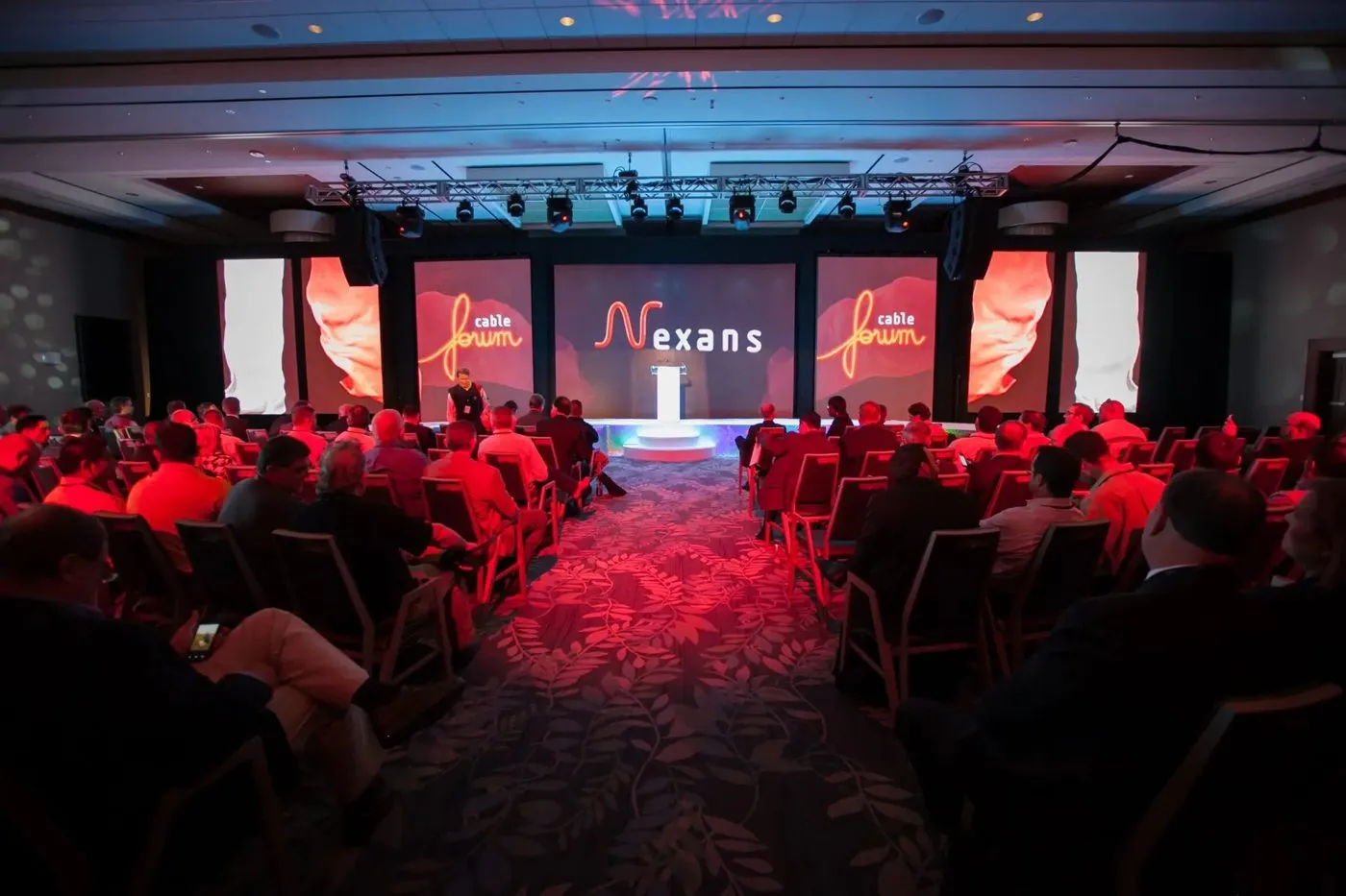 Conference audience facing a lit stage with large screens
