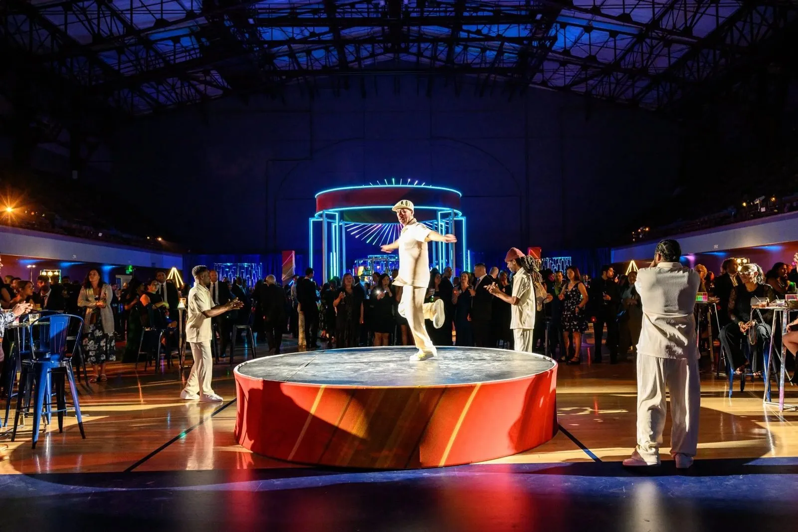 Guests around a lit circular stage in a large event hall
