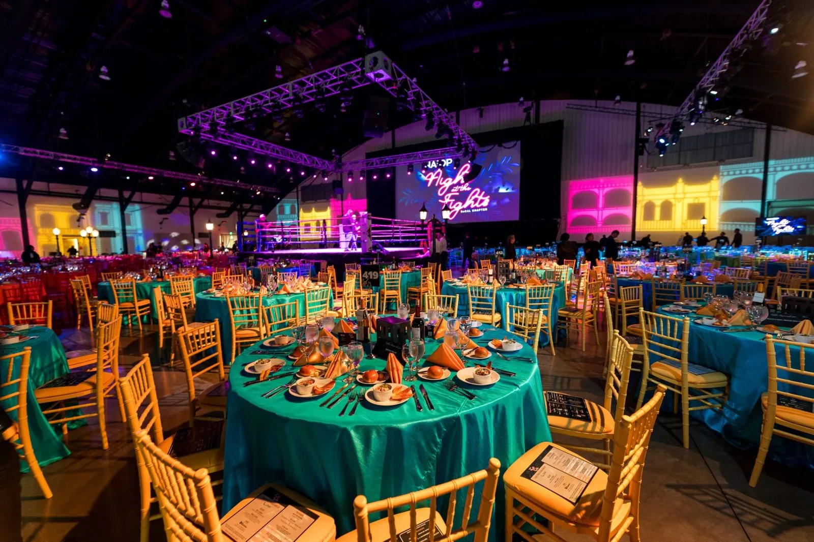 Banquet room with teal tablecloths, overhead truss lighting and screens